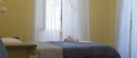 Une chambre Ă coucher avec un lit, une chaise et une fenĂŞtre avec des rideaux.