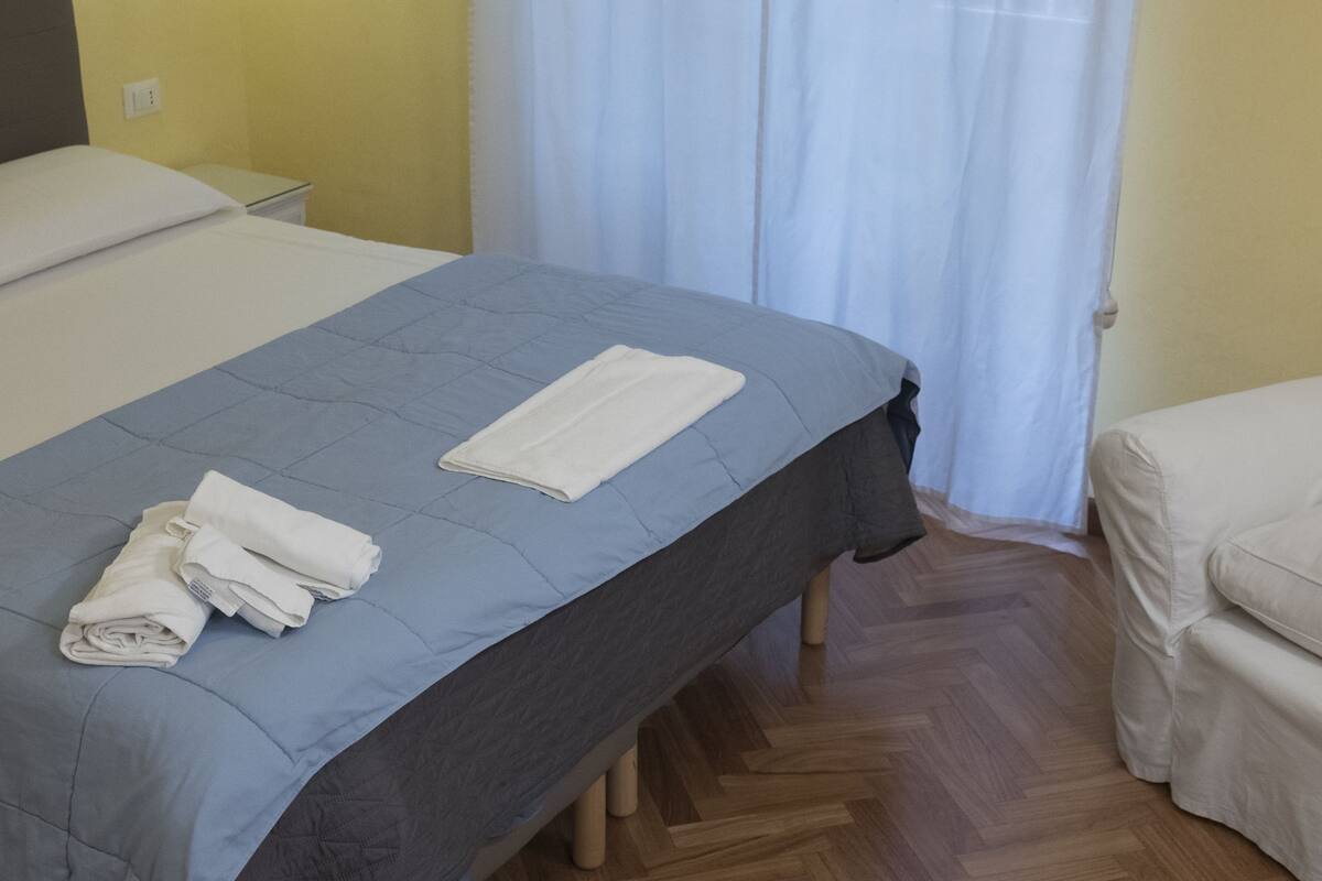 Ein Einzelbett mit blauer Bettdecke, ein sauber gefaltetes weißes Handtuch und ein weißes Kopfkissen.