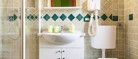 Un baño con ducha, inodoro y lavamanos, con azulejos verde y beige y un espejo sobre el lavamanos.