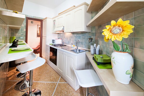 A compact kitchen with white cabinets, a gas stove, a sink, and a large sunflower decoration. - Il Gladiatore (Rome)