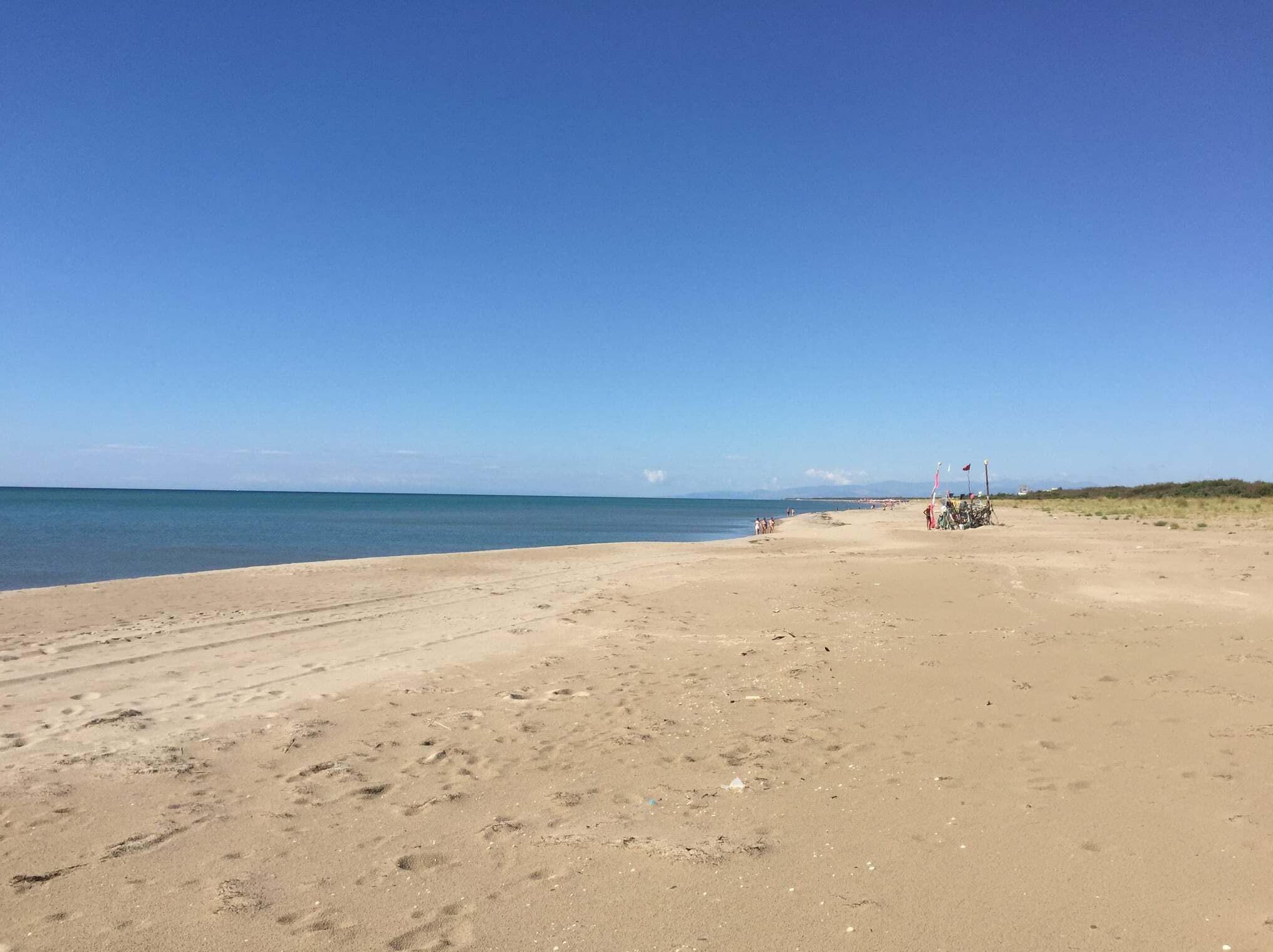 En bred sandstrand med fodspor og et par personer i det fjerne.