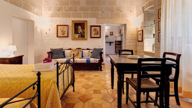 A cozy room with a bed, a wooden table with chairs, a sofa with cushions, and a dining area.