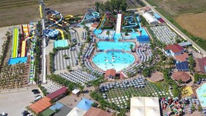 An aerial view of a resort with a central swimming pool, multiple water slides, and numerous sun loungers arranged around the pool area.