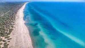 An aerial view of a coastal area with a long stretch of beach and clear blue waters.