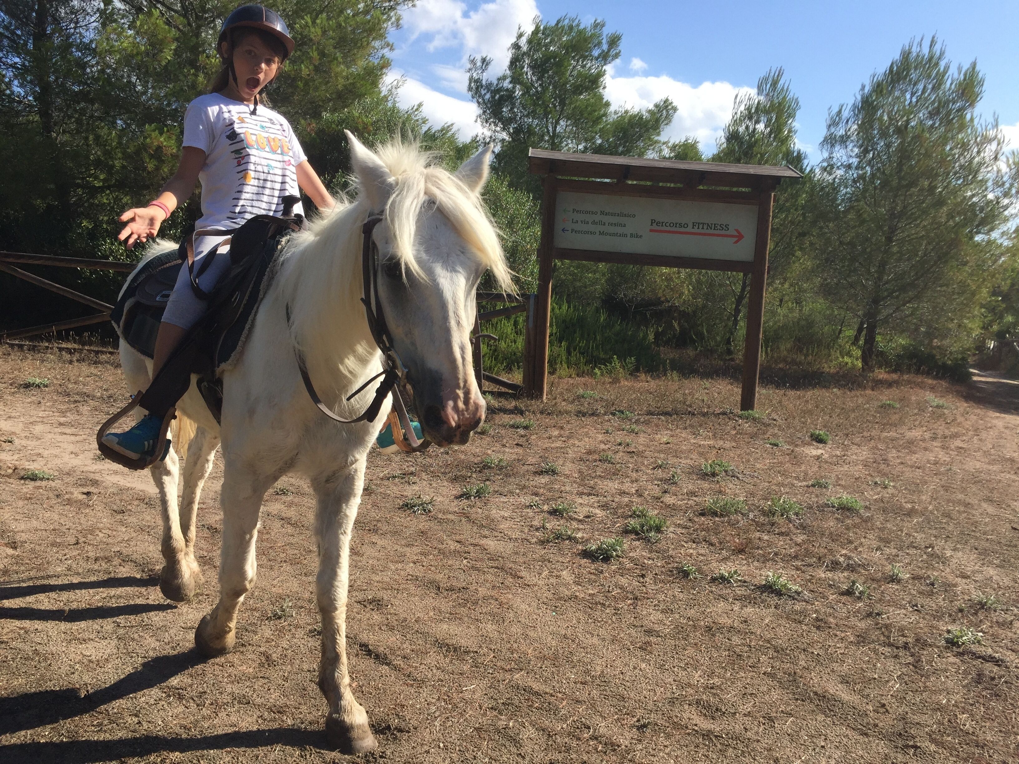 A person riding a horse on a dirt path with a sign indicating directions to various trails.
