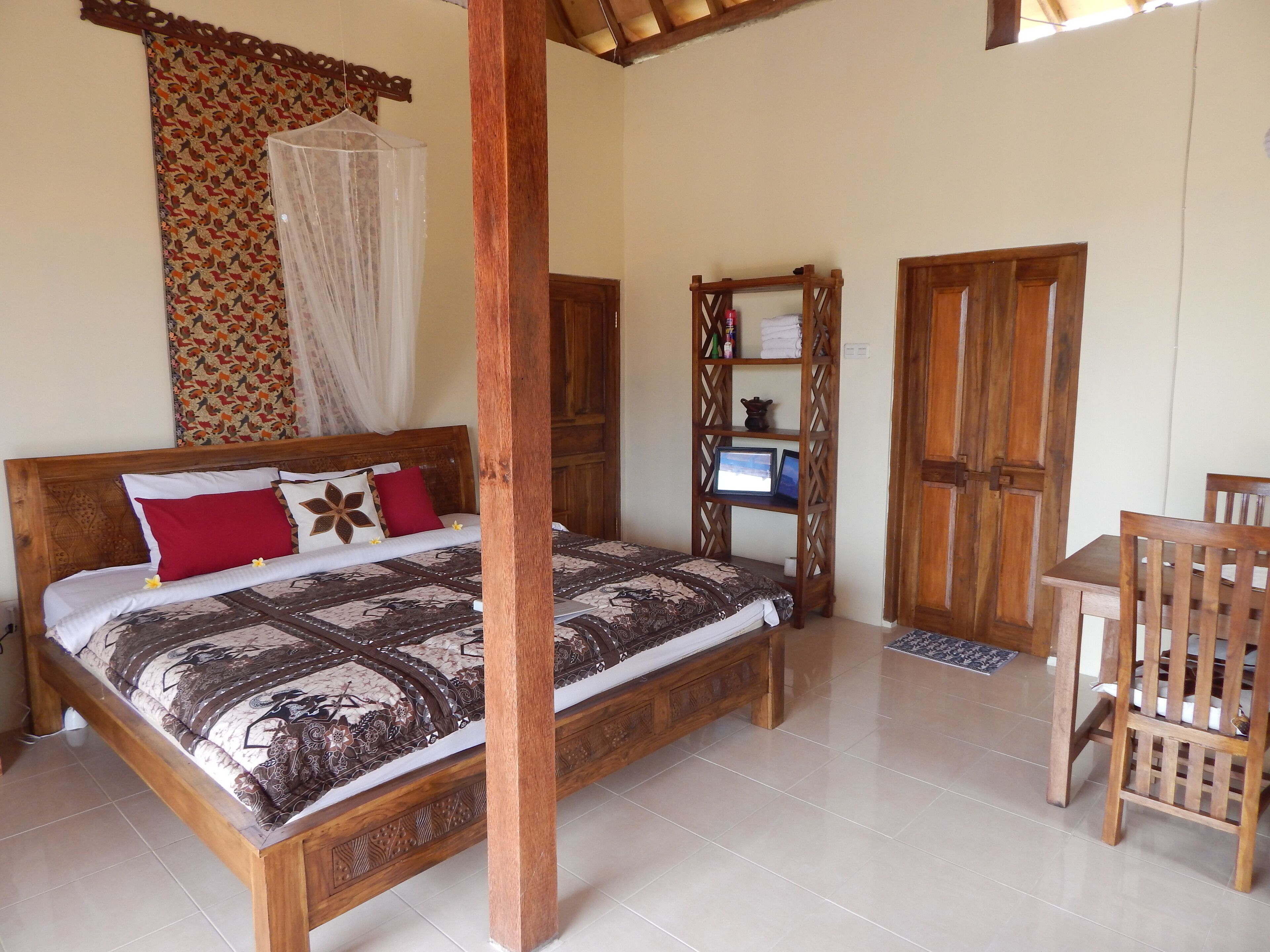 Una cama de madera con una colcha estampada, una silla de madera y una estantería con un ordenador portátil y fotografías enmarcadas.
