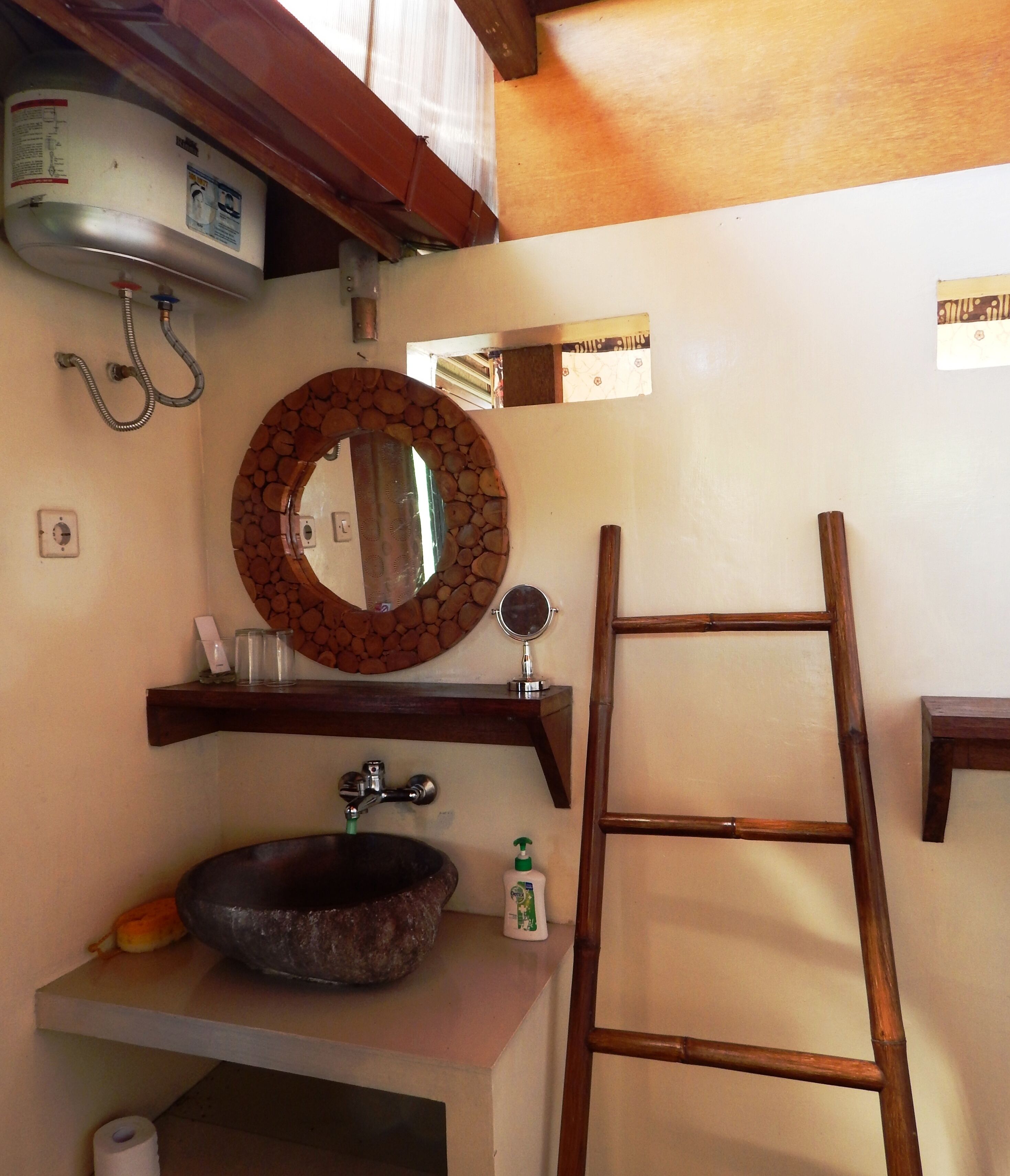 A bathroom with a stone sink, a wooden ladder, a round mirror with a stone frame, and a wooden shelf above the sink.