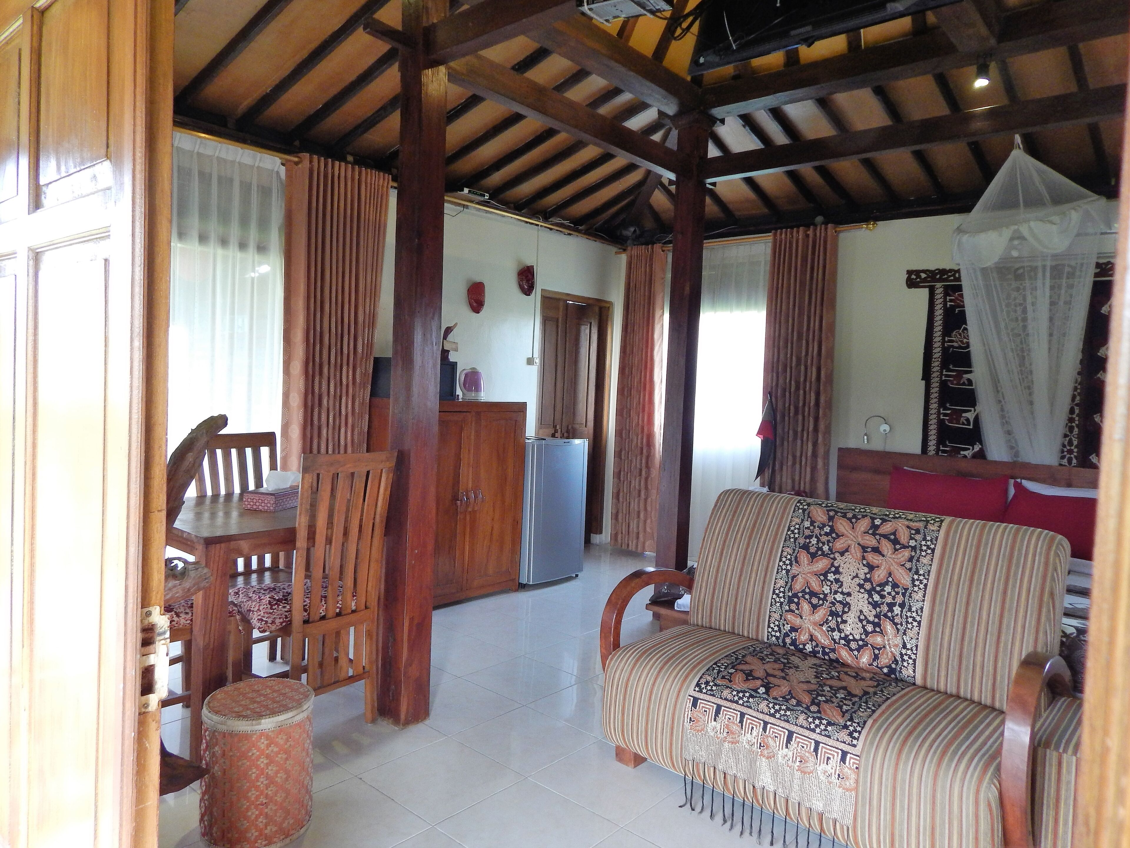 A room with a wooden ceiling, a sofa with a patterned cover, a dining table with chairs, and a cabinet.