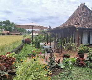 Zona salotto all'aperto coperta, con tavolo e sedie, circondata da piante in vaso e un giardino.