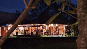 An outdoor restaurant with tables and chairs, surrounded by trees and a stone wall. - Alamanda Family Villas & Pool (Sleman)