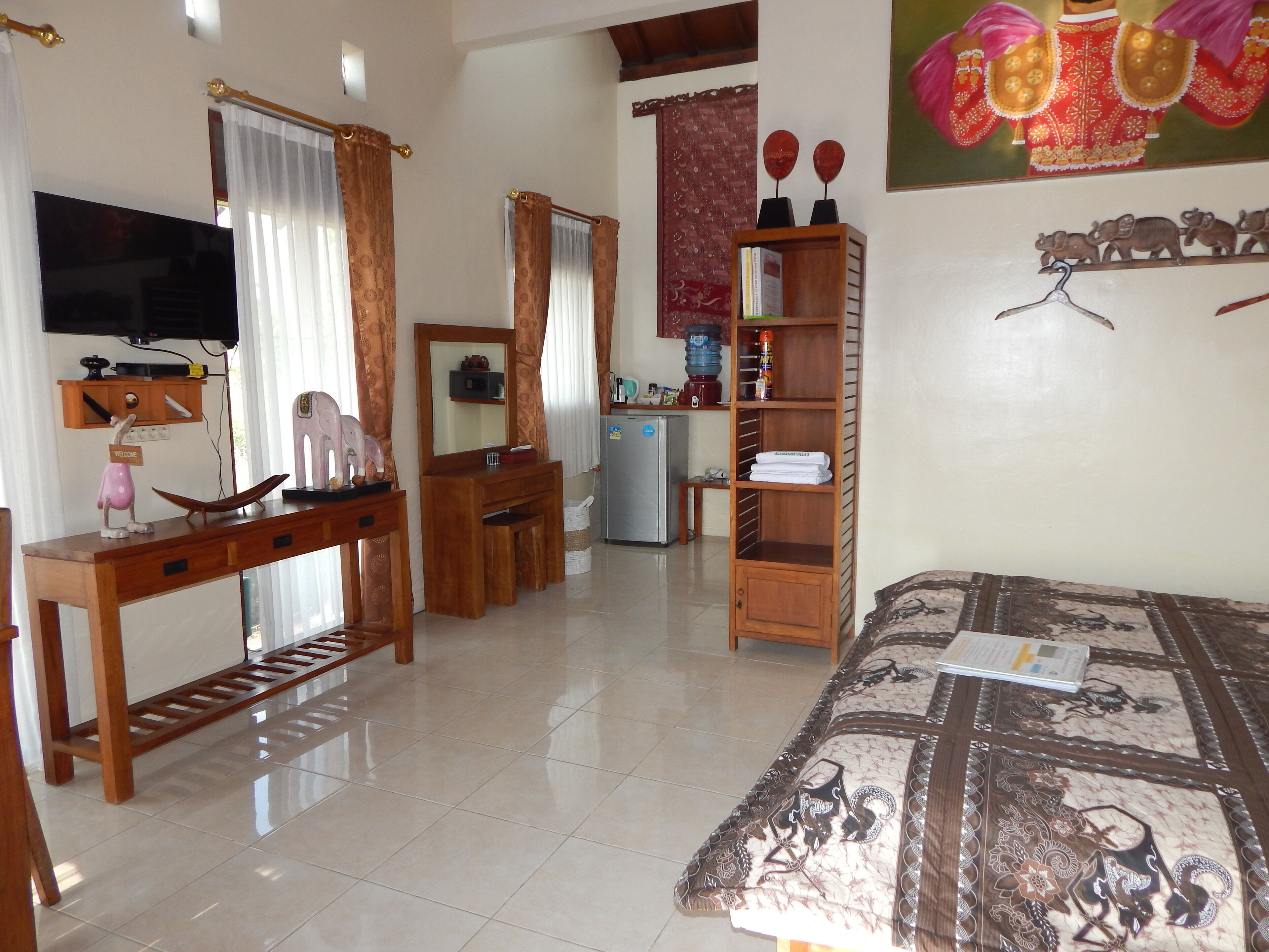 Une chambre d’hôtel comprenant un lit, un bureau en bois, une télévision, une armoire et une étagère avec des serviettes.
