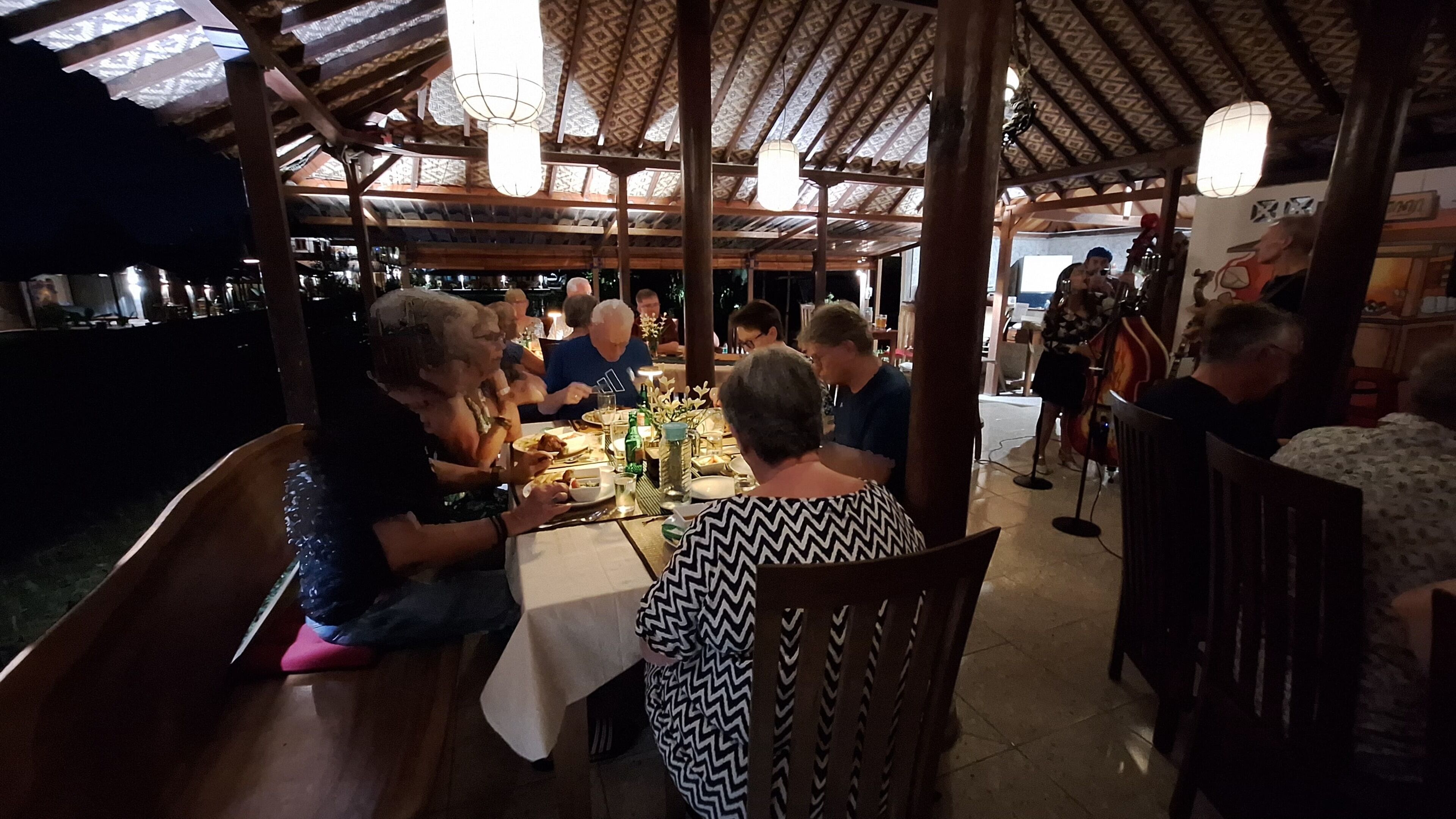 Un restaurante con mesas y sillas de madera, techo con diseño y luces colgantes.