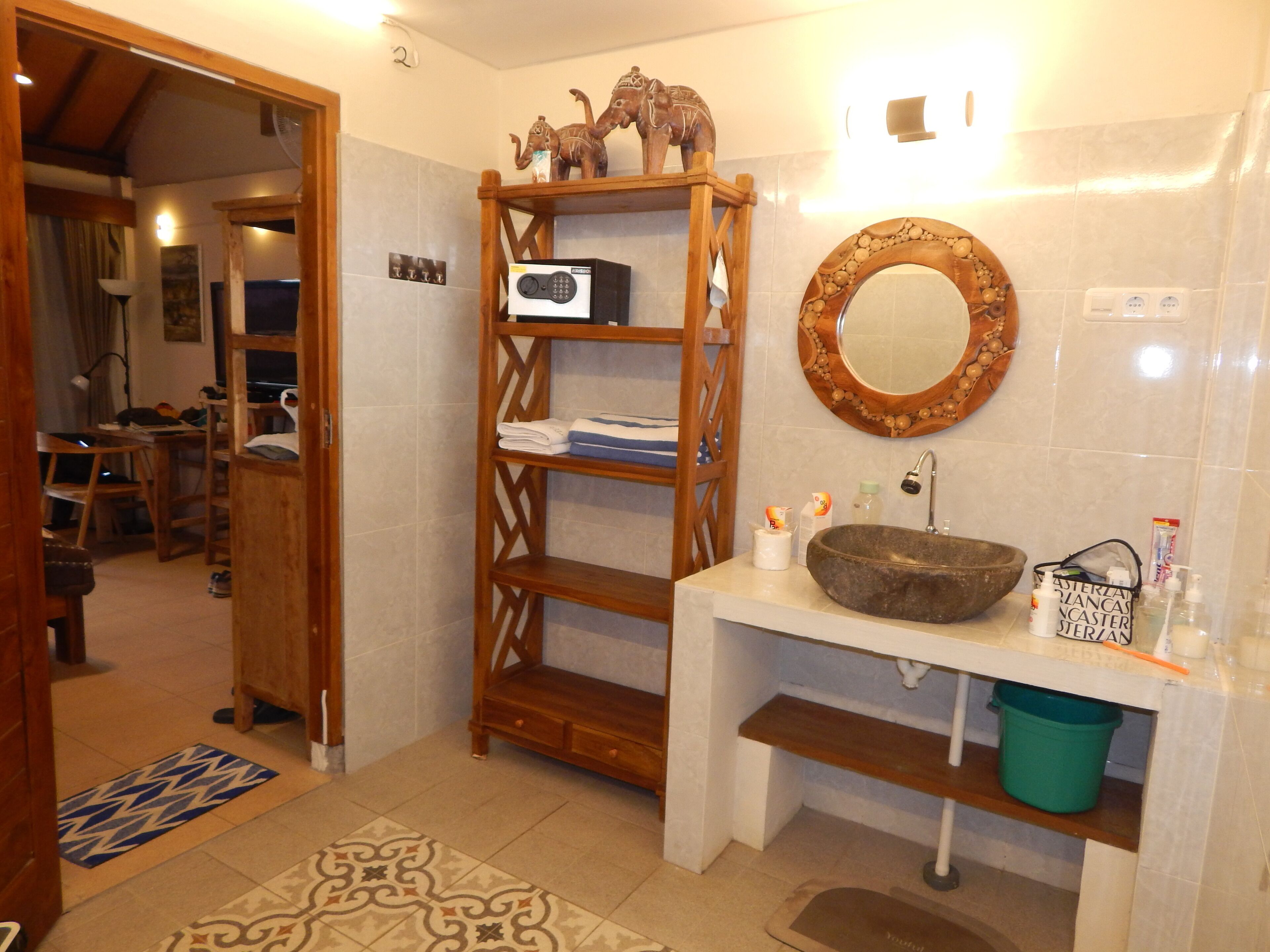 A bathroom with a wooden shelf, a stone sink, and a mirror.