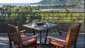 Una terraza de madera con una mesa dispuesta para el desayuno, con vista a un lago y colinas.