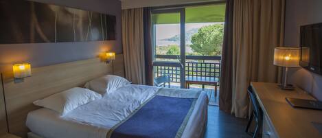 A hotel room with a bed, bedside lamps, a desk with a laptop, and a view of the outdoors.