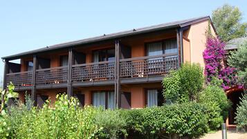 A multi-story hotel with balconies, surrounded by greenery and a flowering bush.