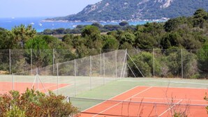 Cancha de tenis con red, rodeada de árboles y montañas al fondo.