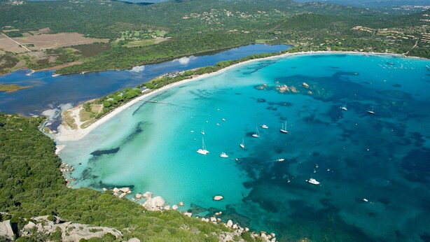 Vista aérea de una zona costera con aguas turquesas cristalinas, barcos y una playa.