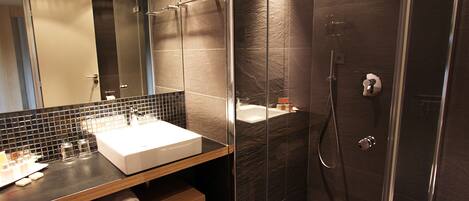 Un baño moderno con ducha envuelta en vidrio, un lavabo blanco y un mueble de tocador de madera.