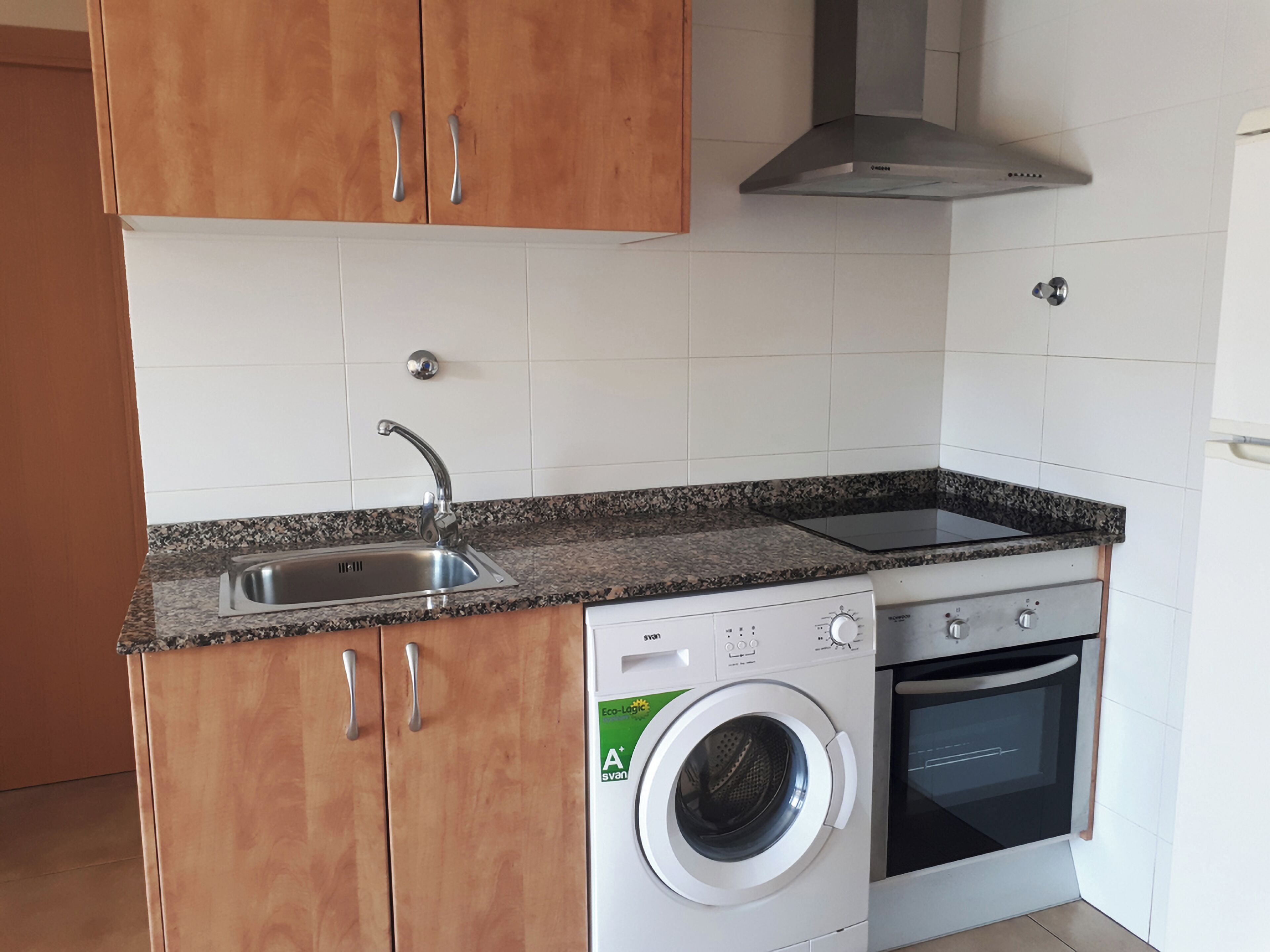 Cozinha compacta com máquina de lavar embutida, fogão e pia.