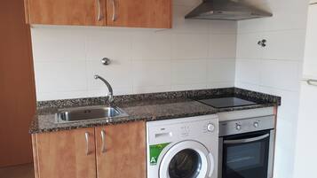 Una cocina compacta con lavadora integrada, estufa y lavabo.