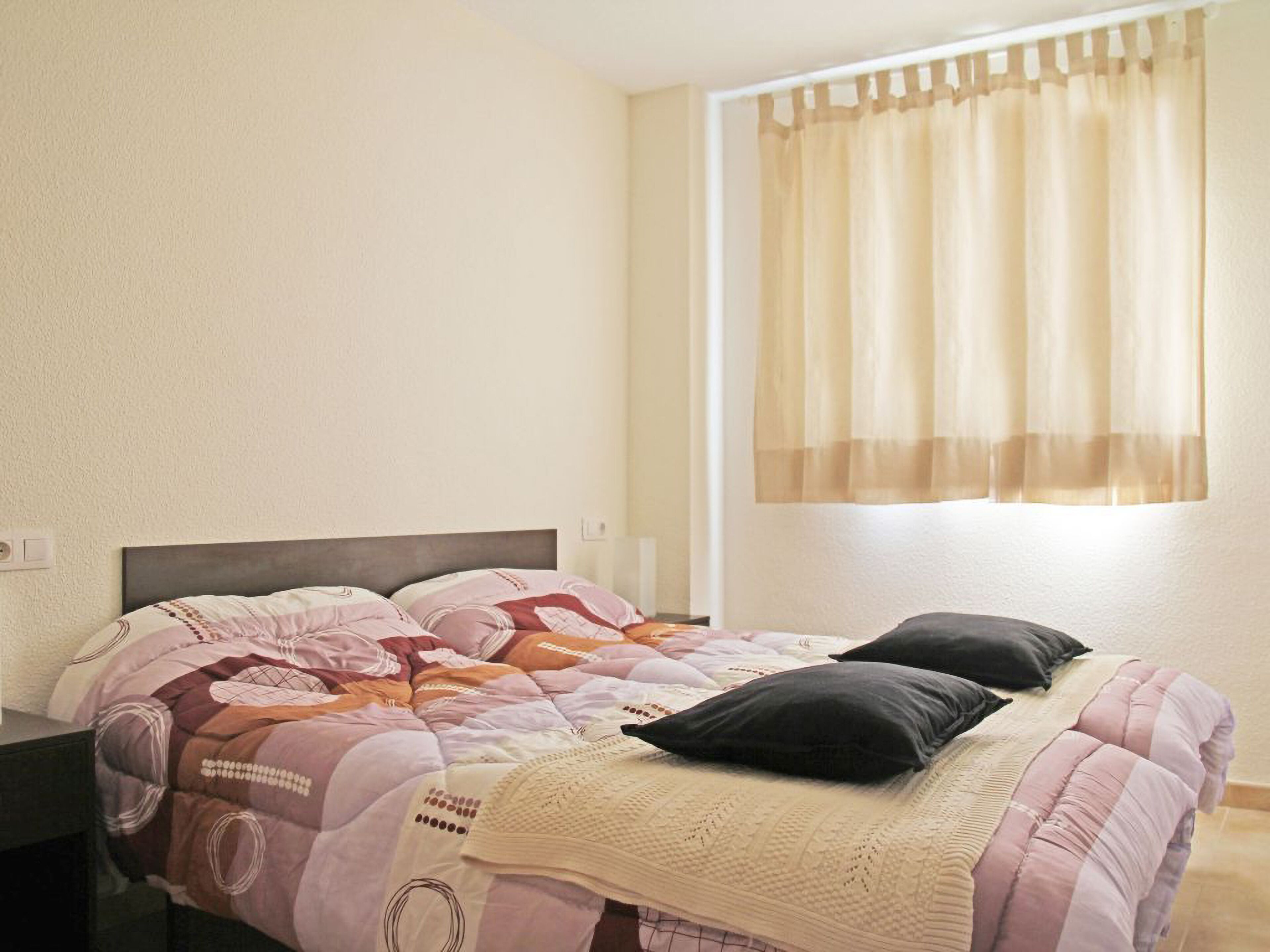 A bedroom with a bed, a nightstand, and a window with curtains.