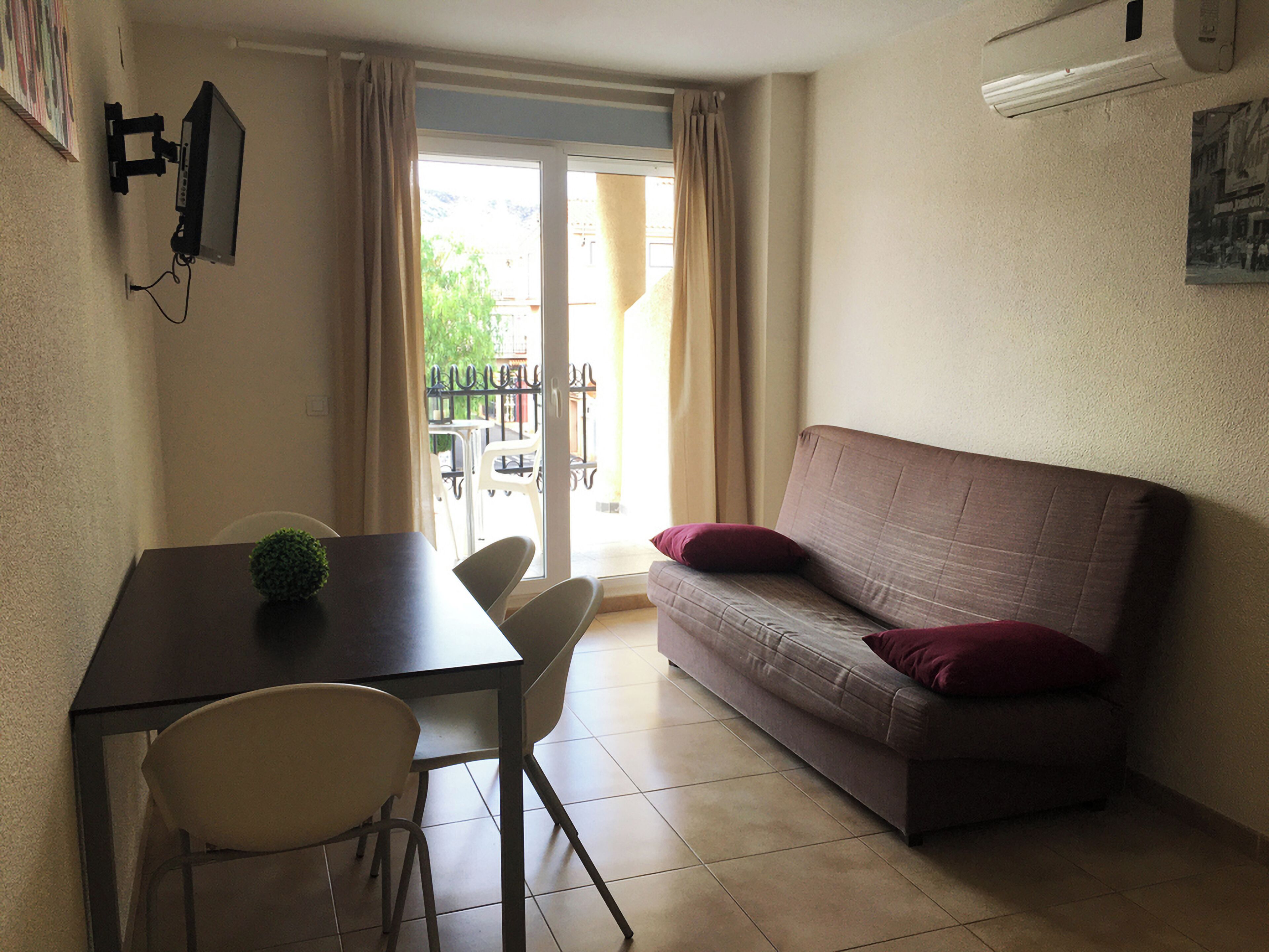 Una sala pequeña con un sofá, dos sillones, una mesa y un televisor montado en la pared.
