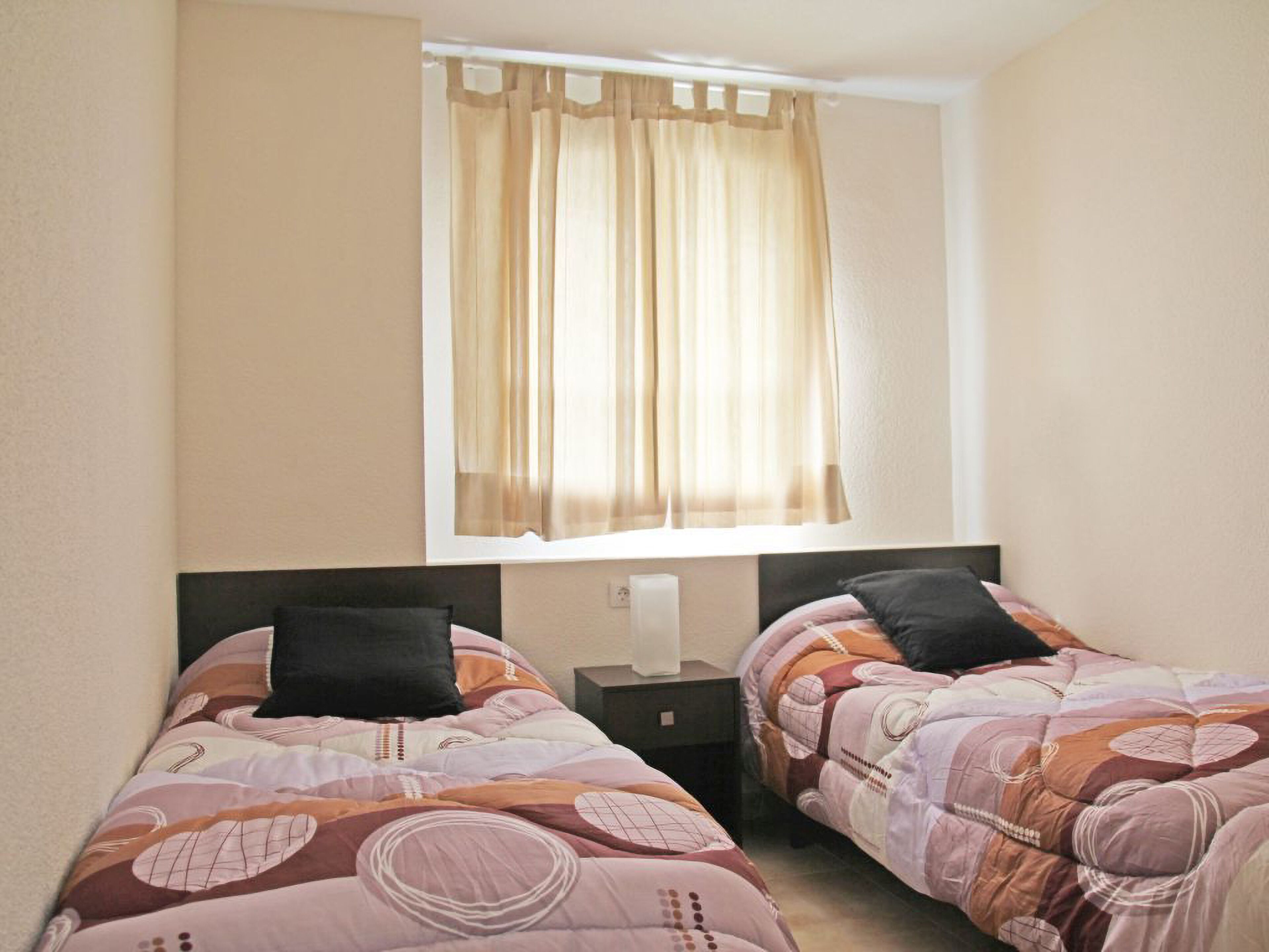 Une chambre double avec deux lits, une fenêtre avec des rideaux légers et une table de chevet avec une lampe.