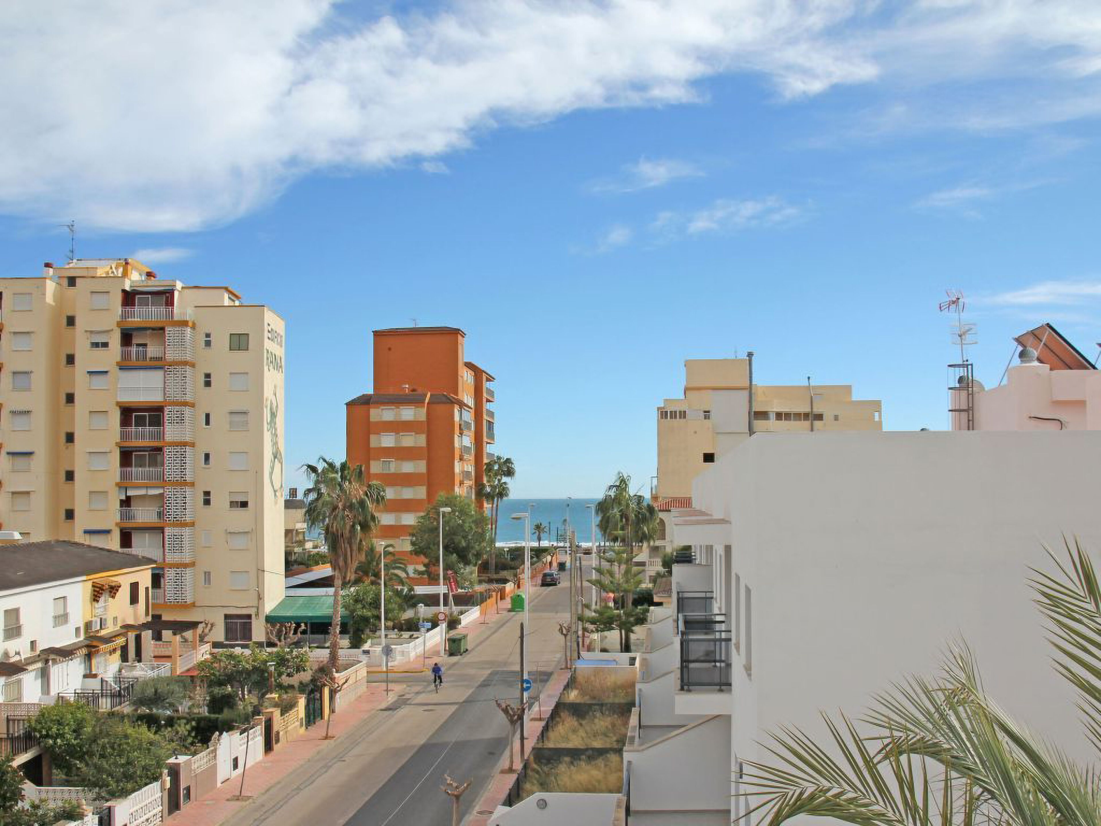 Une rue urbaine située sur la côte, bordée d’immeubles à plusieurs étages, dont un bâtiment orange remarquable et un bâtiment blanc doté de balcons.