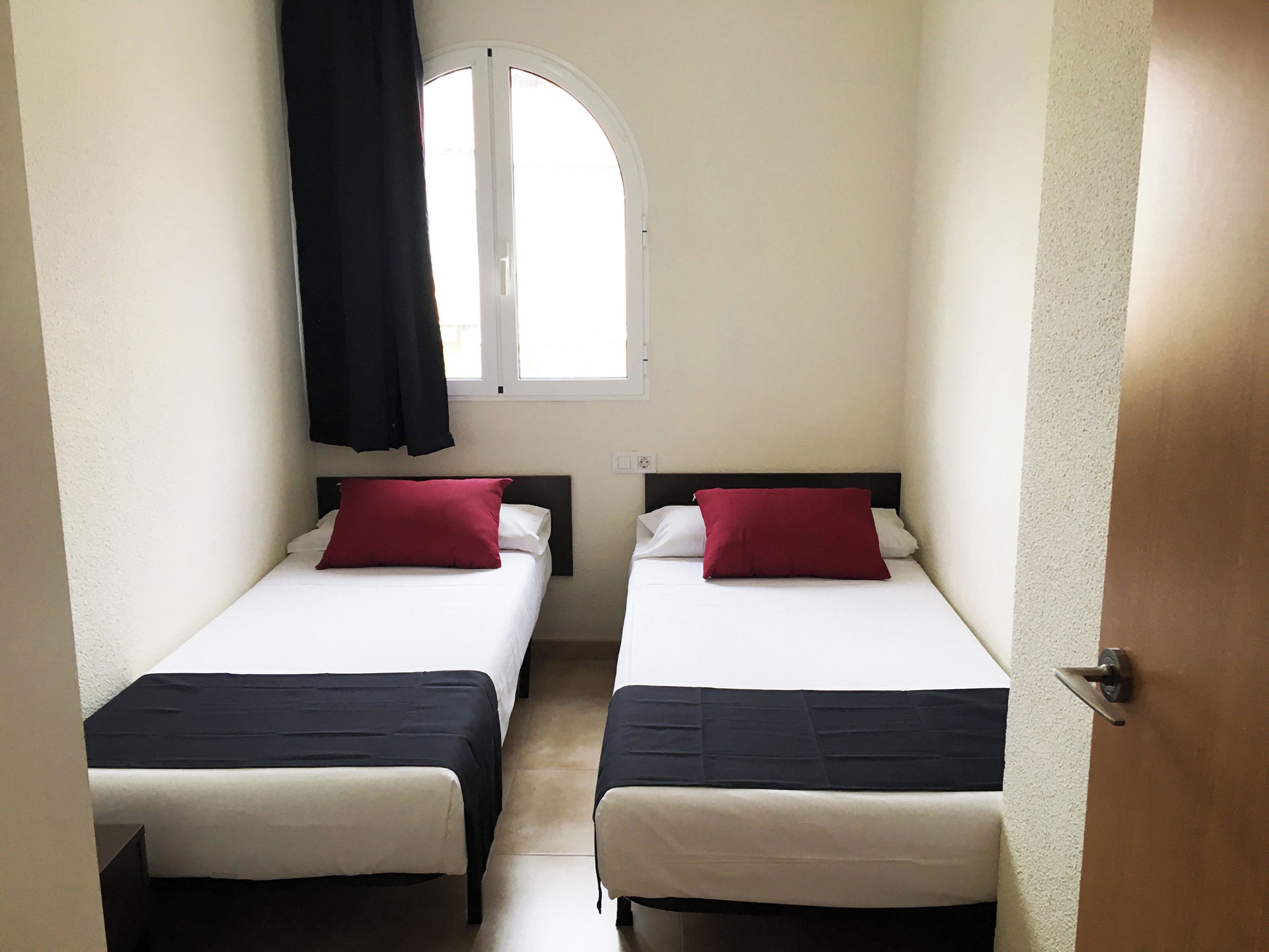 Una habitación con dos camas, cada una con cabecero negro y ropa de cama blanca, y almohadas rojas.