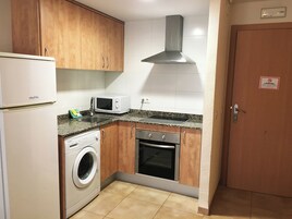 A compact kitchen with wooden cabinets, a microwave, a washing machine, and an oven.