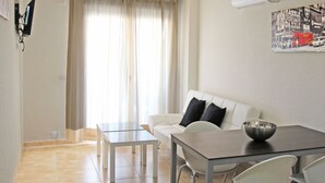 A modern living room with a white sofa, a glass coffee table, and a dining table with chairs. - Apartamentos Doña Carmen 3000 (Oropesa del Mar)
