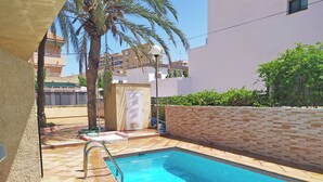 A swimming pool with a tiled deck, a palm tree, and a building in the background. - Apartamentos Doña Carmen 3000 (Oropesa del Mar)