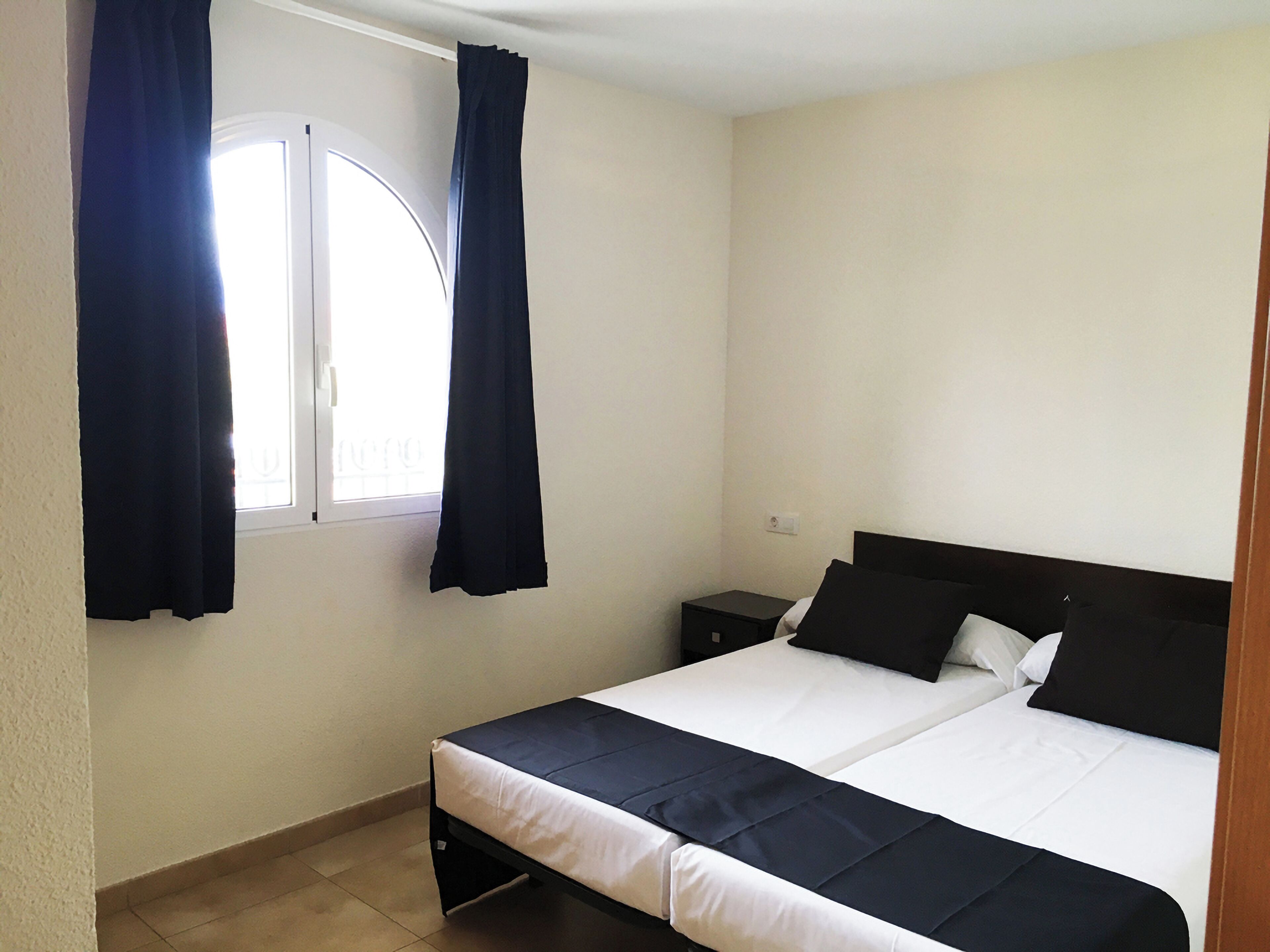 Un dormitorio con una cama, una mesita de noche y una ventana con cortinas.
