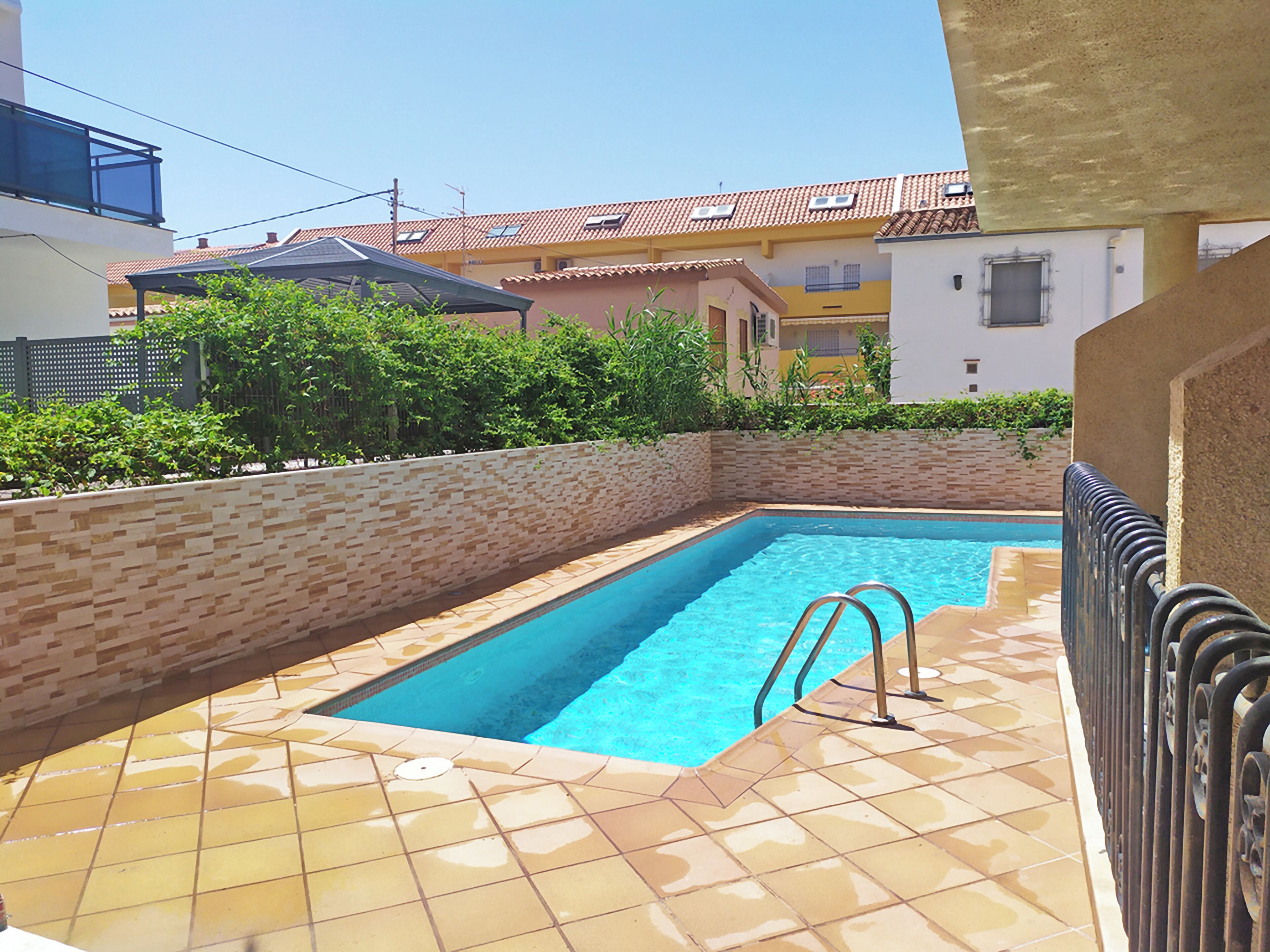 A rectangular swimming pool with a tiled deck, surrounded by a low brick wall and greenery.