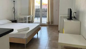 A hotel room with a bed, a desk, a chair, a TV, and a balcony with a view of the outside. - Apartamentos Doña Carmen 3000 (Oropesa del Mar)