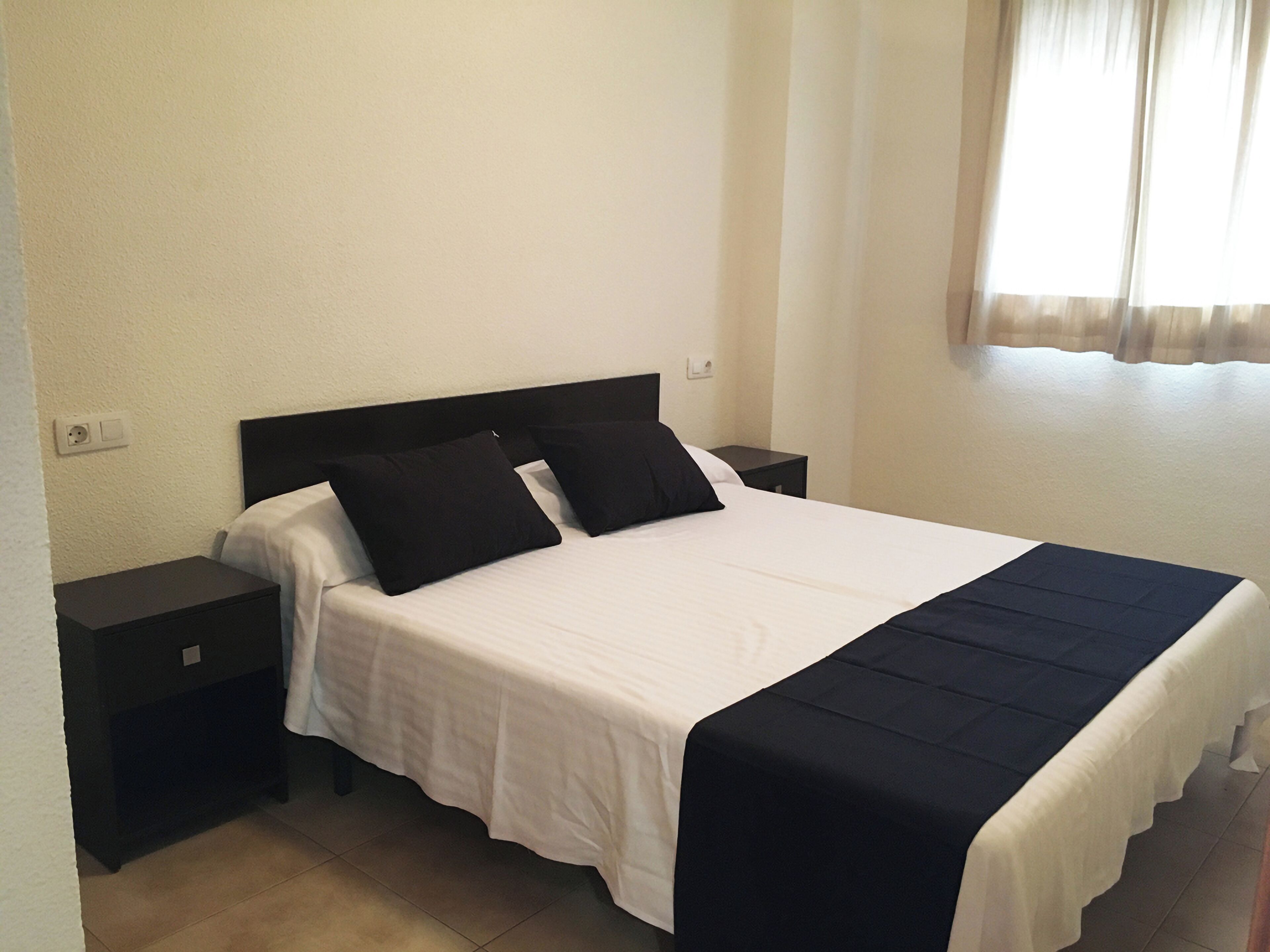 A neatly made bed with a white and black bedspread, two black pillows, and a black nightstand beside it.