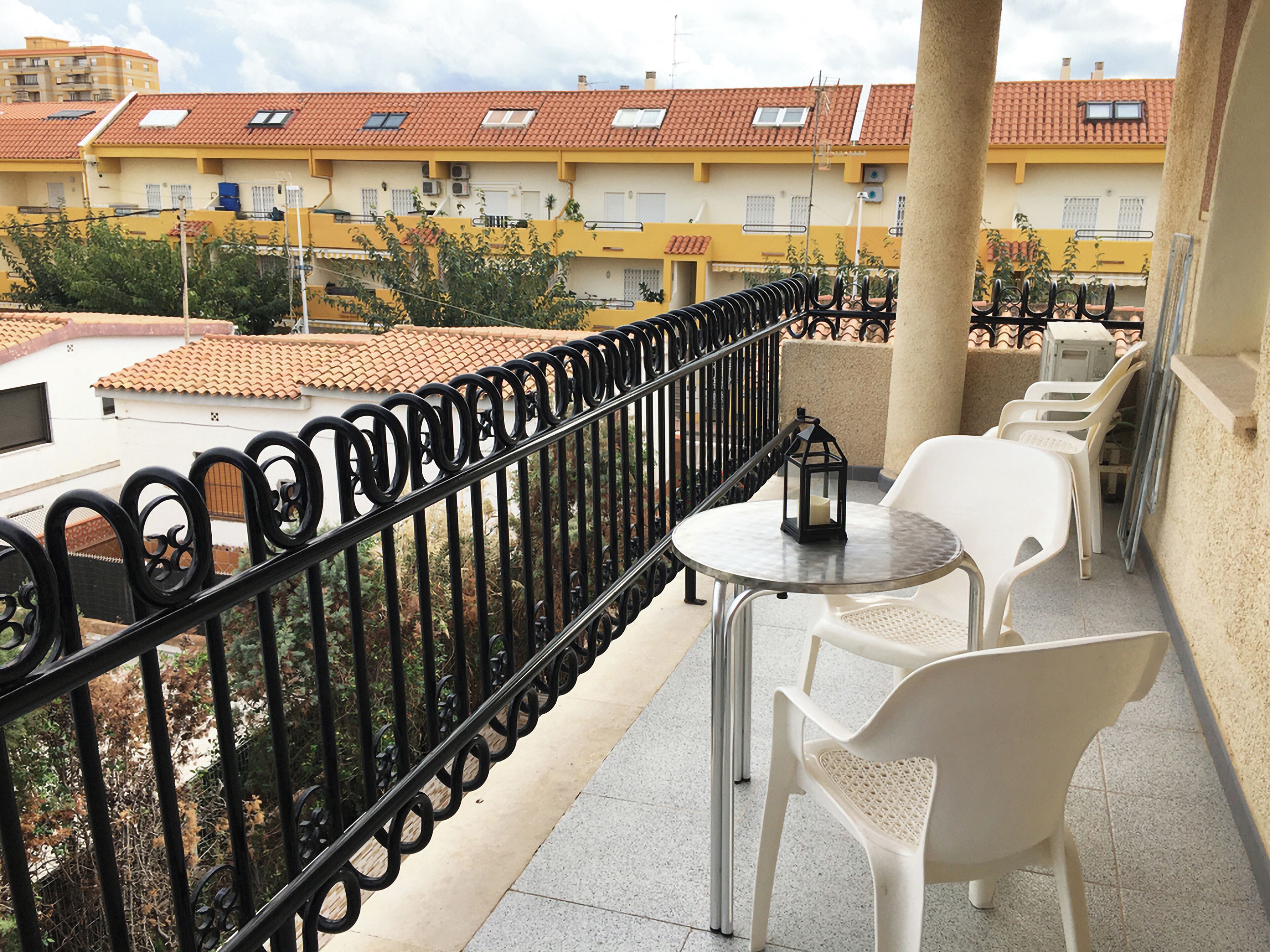 A balcony with a metal railing, a small round table, and white plastic chairs.