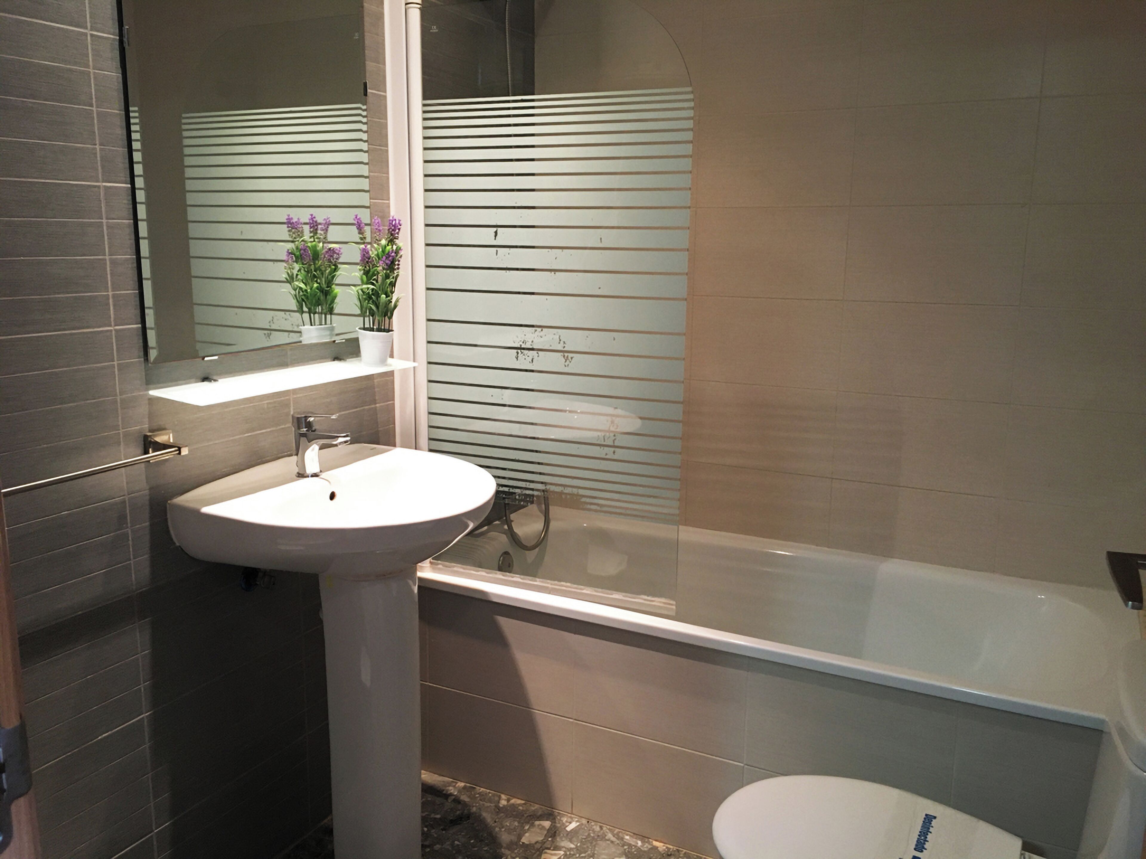 Un baño moderno con lavamanos blanco, un espejo y una bañera.