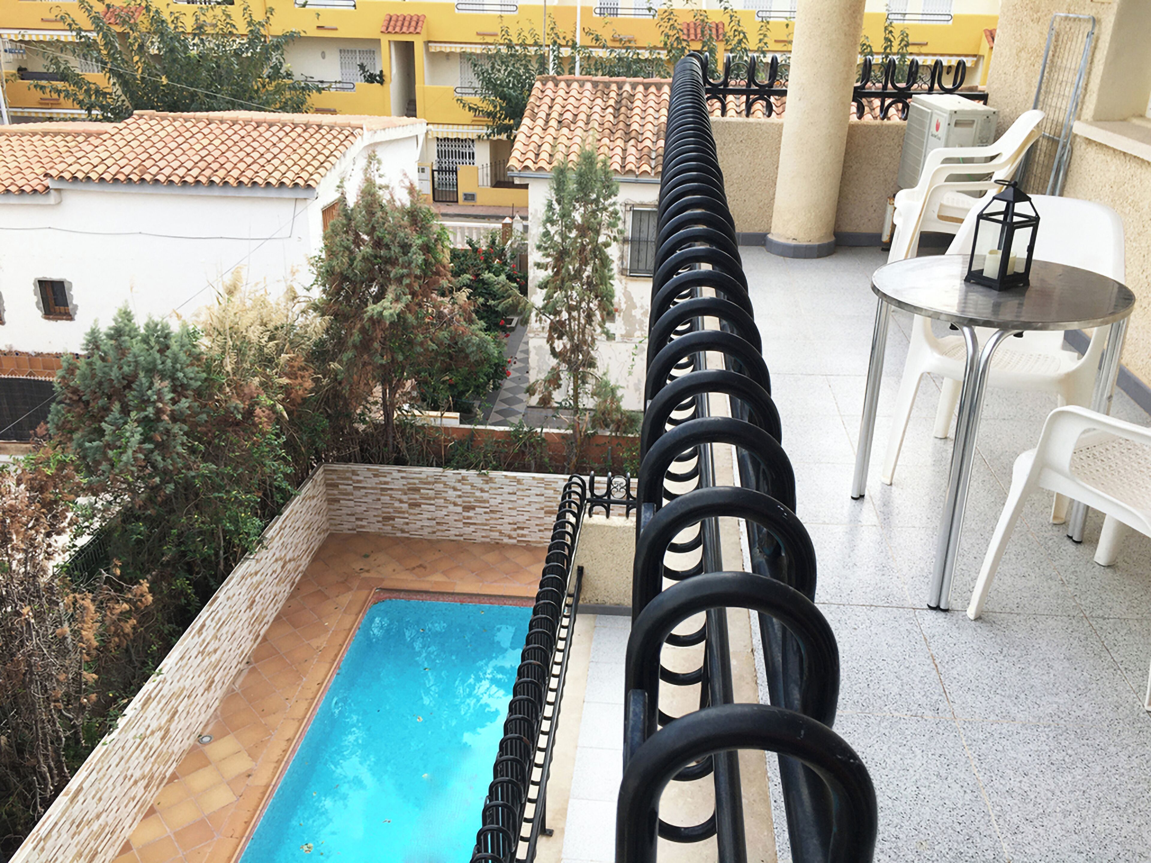 Un área de piscina en la azotea con vista despejada de los edificios circundantes y un conjunto de sillas y una mesa de plástico blanco.