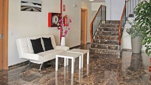 A modern lobby with a white sofa, a small table, a staircase, and a fire extinguisher mounted on the wall. - Apartamentos Doña Carmen 3000 (Oropesa del Mar)