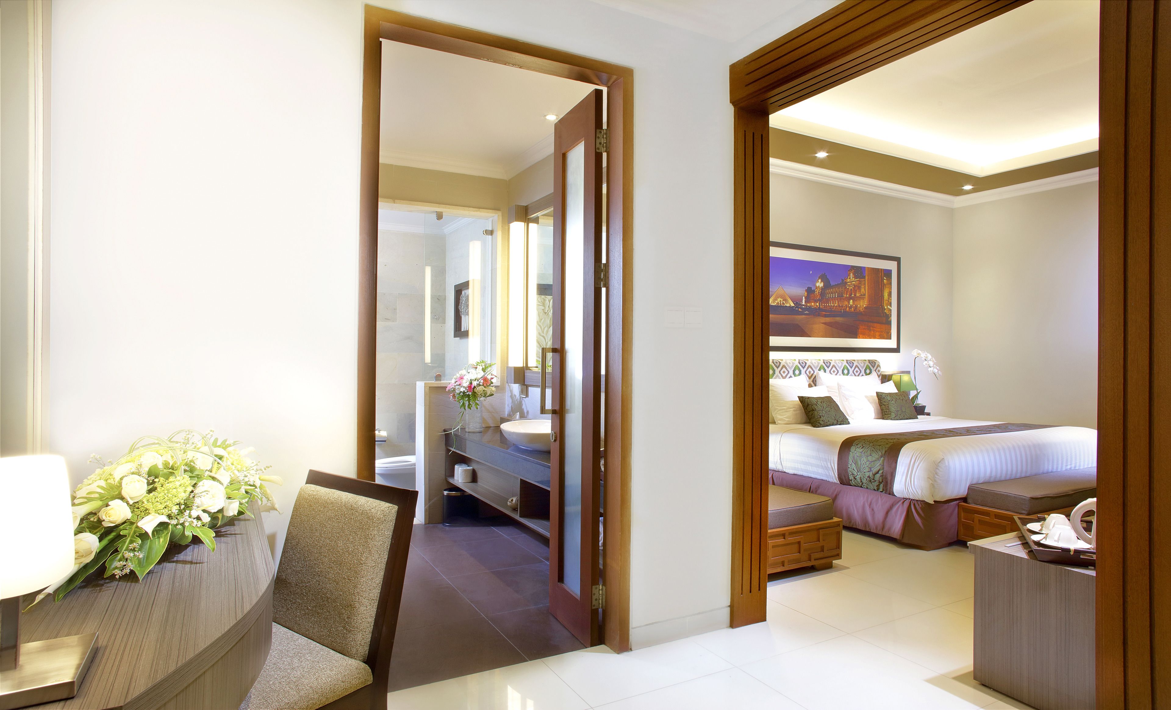 Een hotelkamer met een bed, nachtkastje, stoel, en een badkamer zichtbaar door een geopende deur.