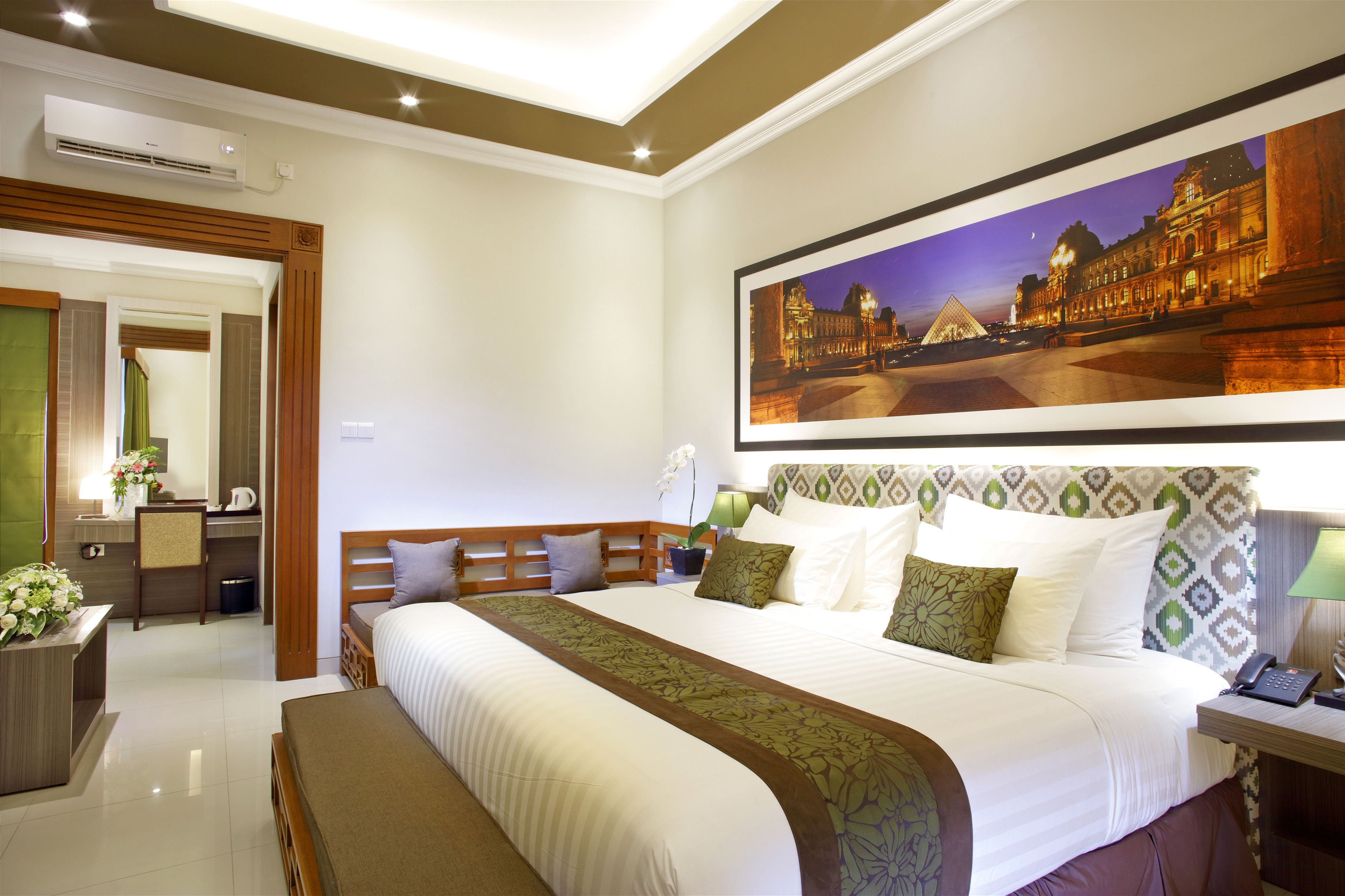 A hotel room with a large bed, a desk, a chair, a mirror, and a framed picture of a building.