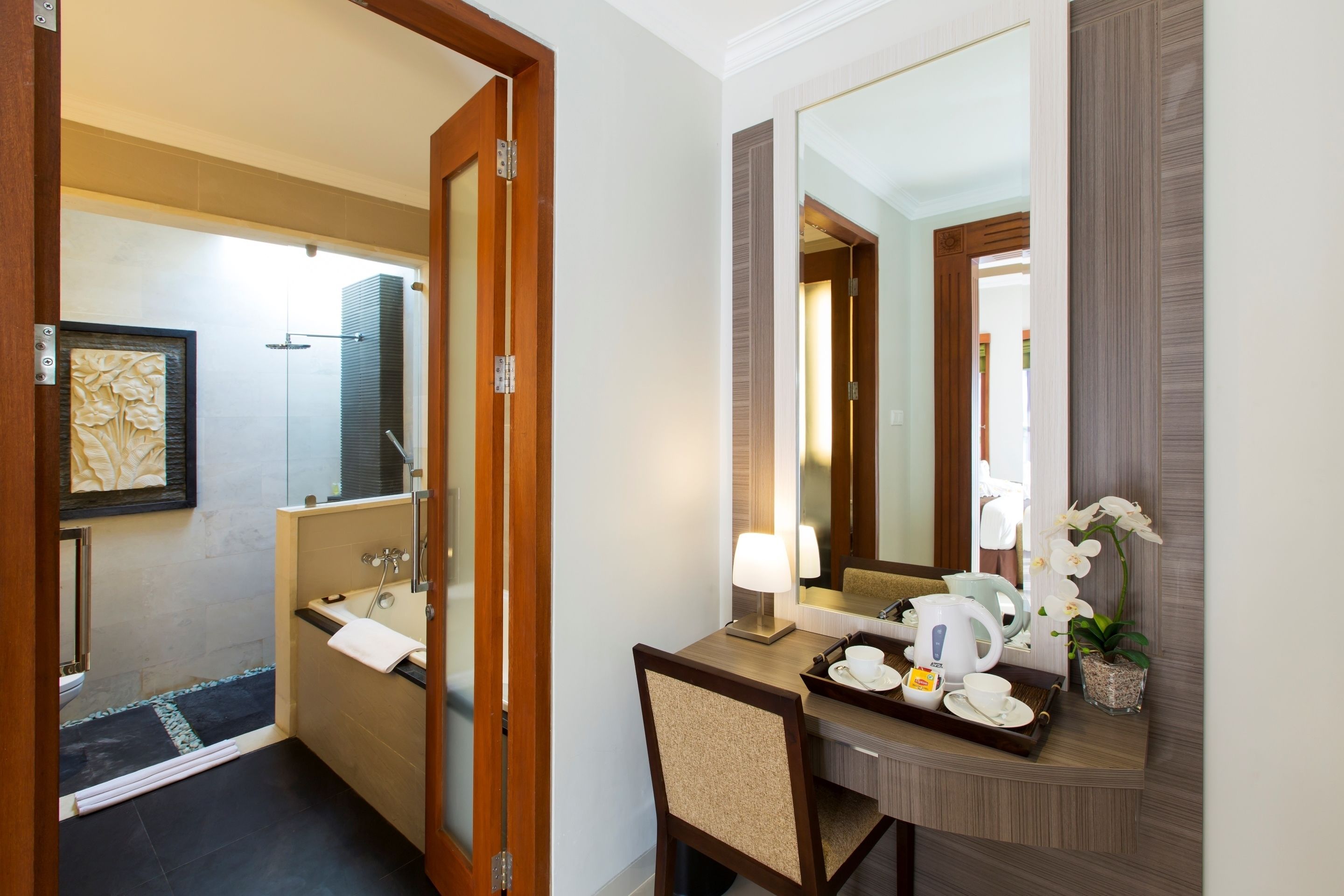A hotel bathroom with a shower, sink, and toilet. There is a mirror, a towel rack, and a tray with cups and a kettle.