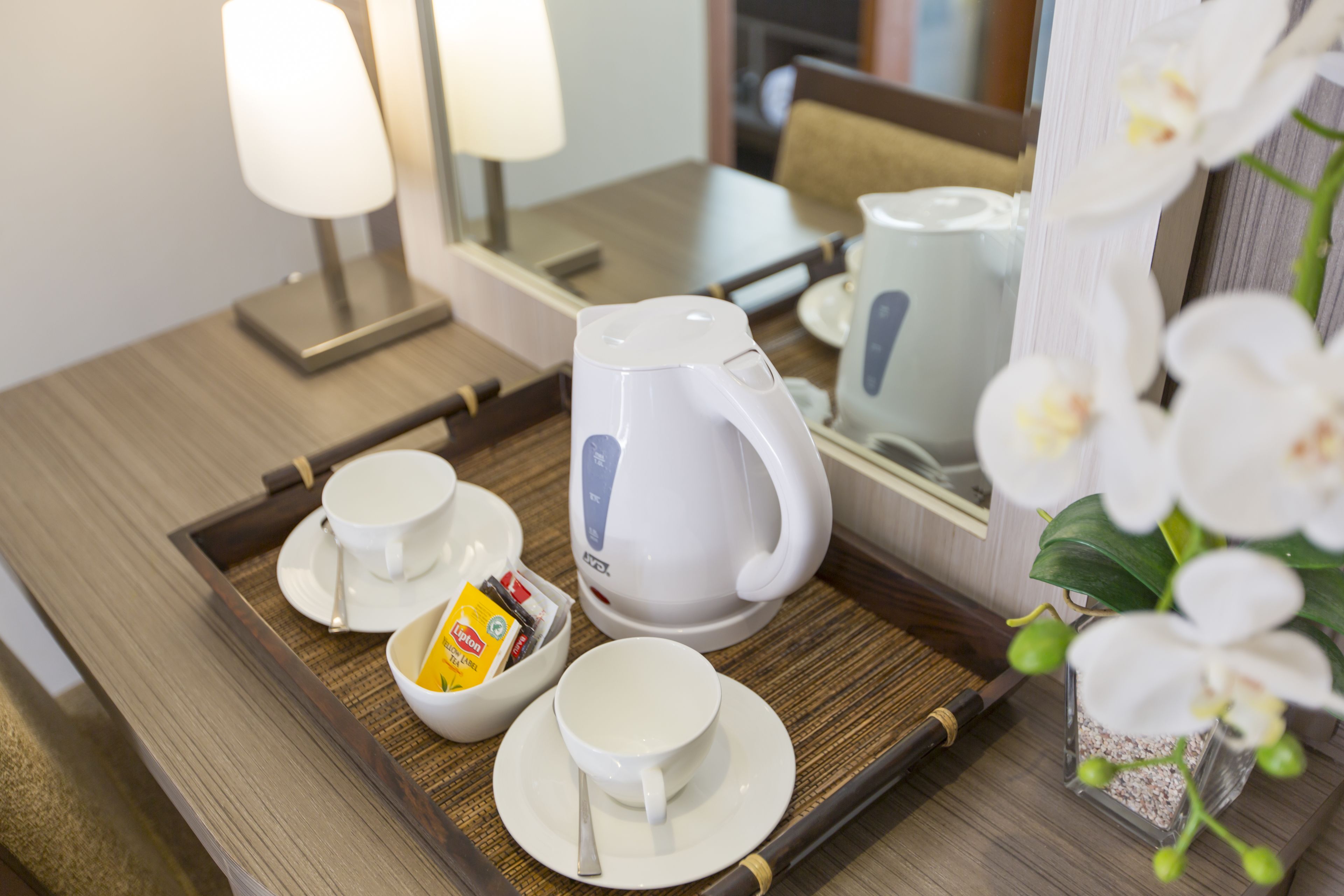 A tray with a tea kettle, cups, and a bowl of snacks on a wooden table.