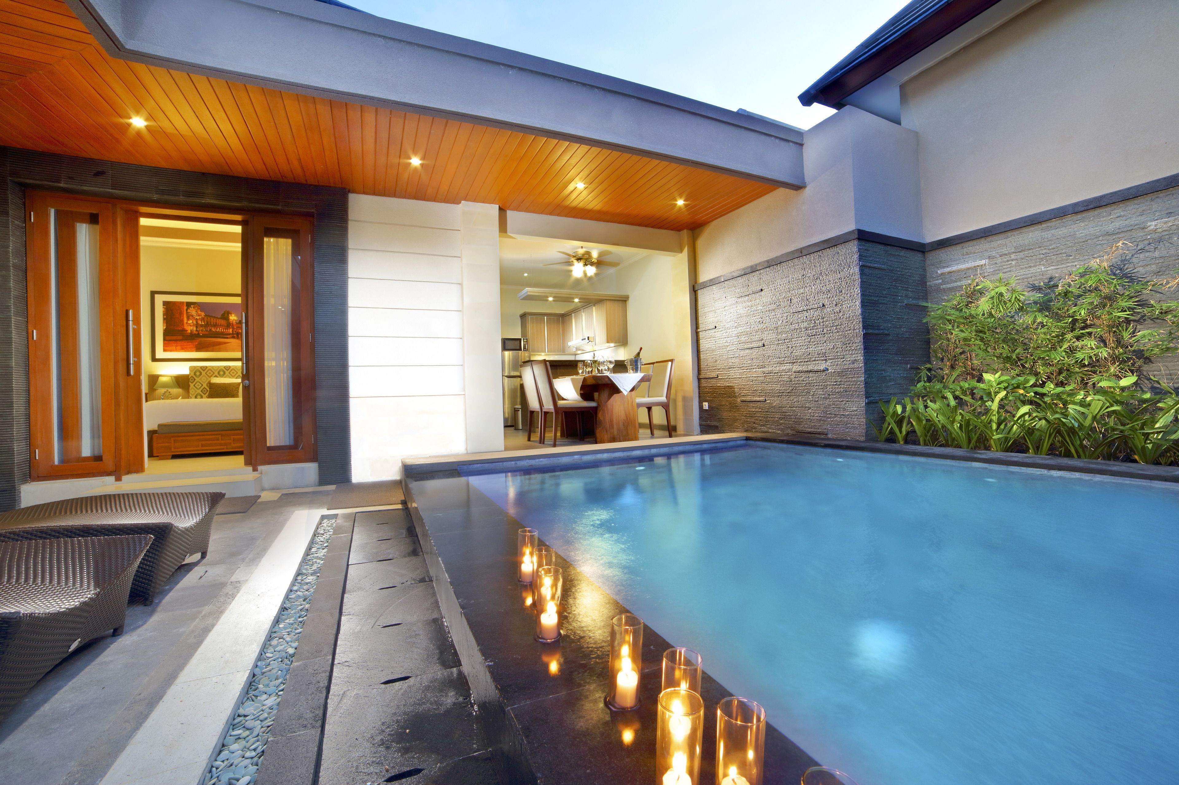 Un área de piscina moderna con techo de madera, zona de comedor y vista a la cocina.