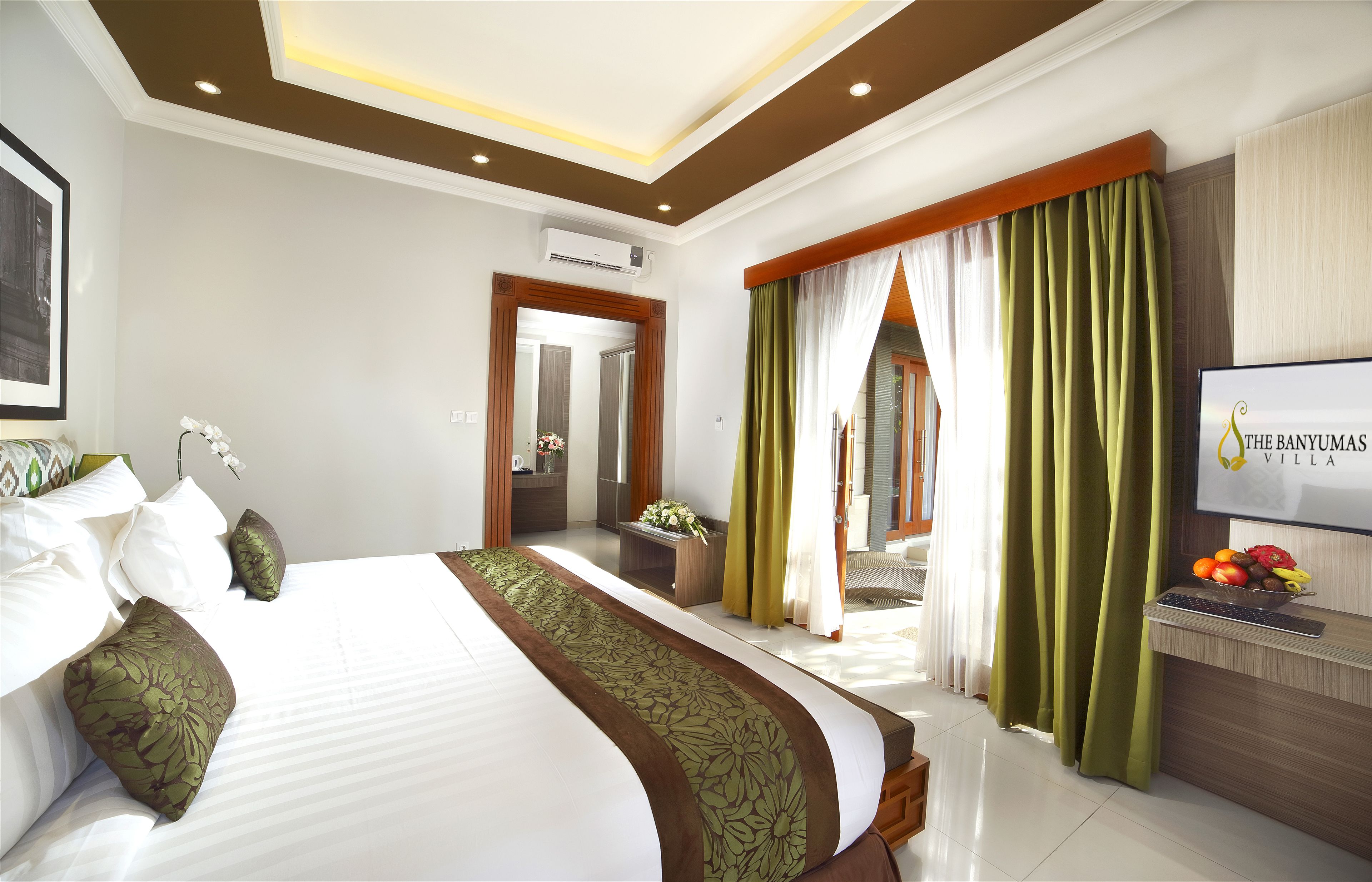 A hotel room with a large bed, a desk with a fruit bowl, and a TV on the wall.