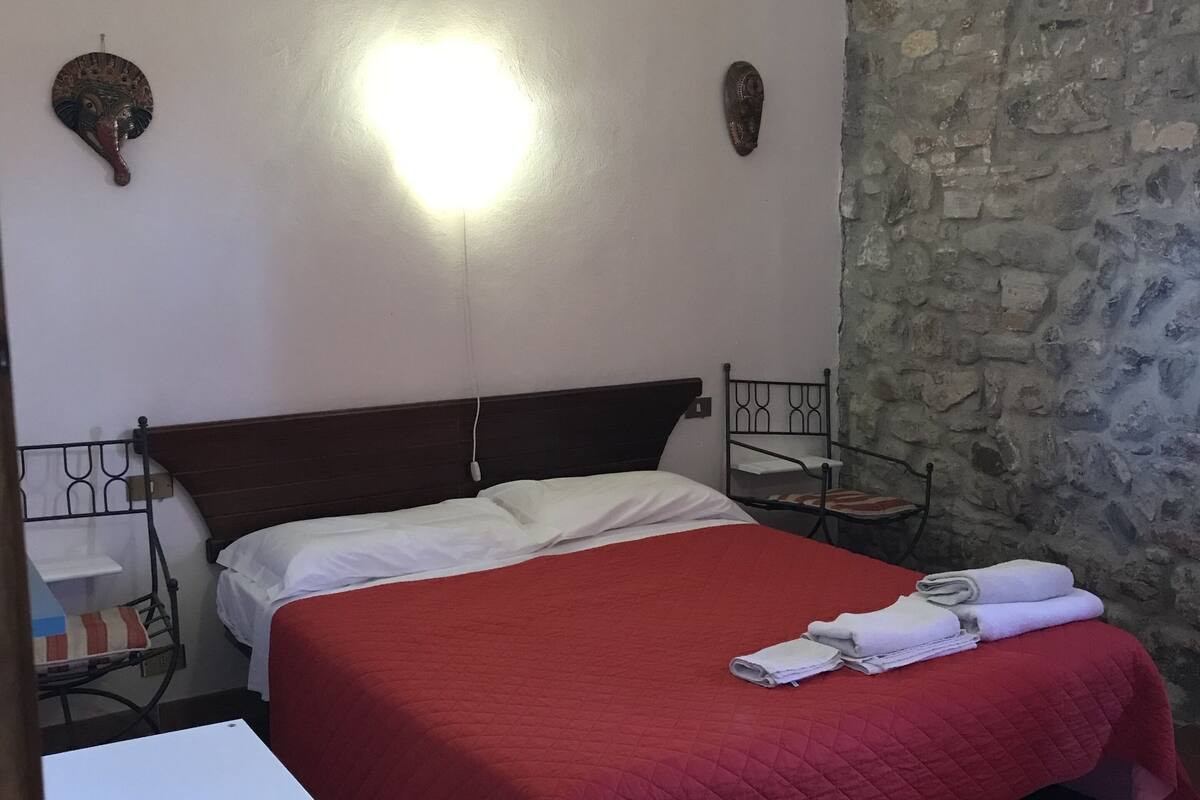Une chambre à coucher avec un lit, une table de chevet, une chaise et un mur en pierre.