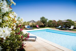 A swimming pool with lounge chairs and umbrellas, surrounded by greenery and flowers.