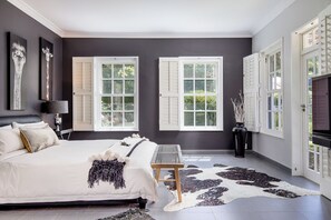 A bedroom with a bed, two windows with shutters, a bedside table, a lamp, and a cowhide rug. - 14 on Klein Constantia (Cape Town)